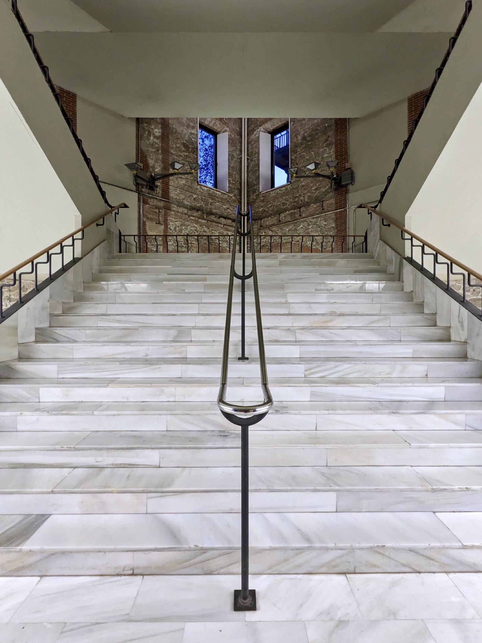 A marble staircase with a central metal railing. In the far back, some bricks from the outer wall are shown.